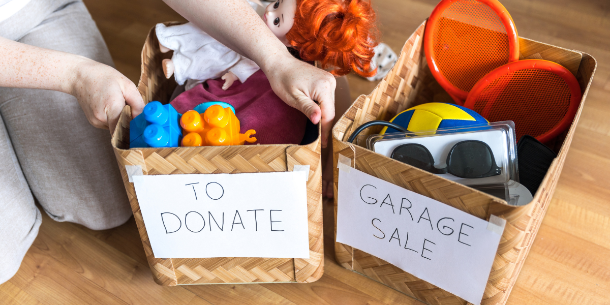 Close-up of baskets labeled "TO DONATE" and "GARAGE SALE" filled with toys and sunglasses, showing how to sort items during a 30-day declutter challenge.